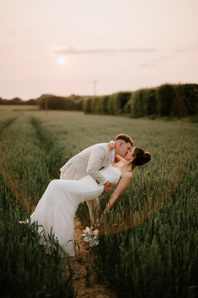Couple on their wedding day kissing in field at sunset at the old kent barn