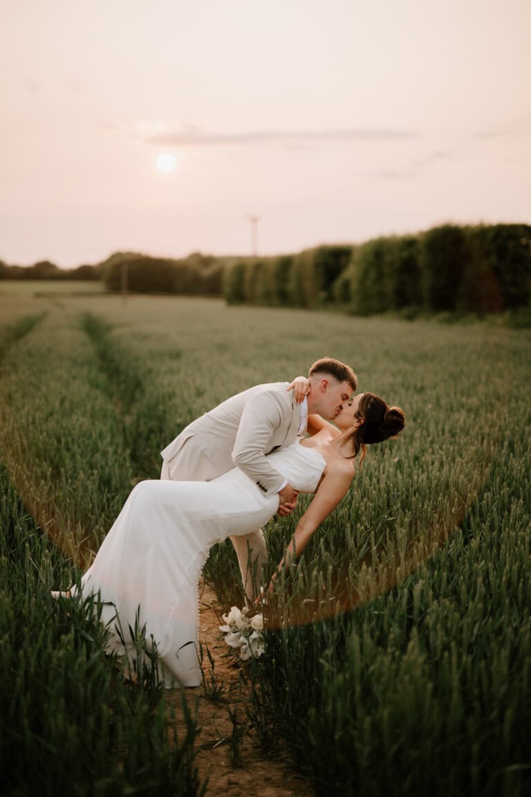Couple on their wedding day kissing in field at sunset at the old kent barn