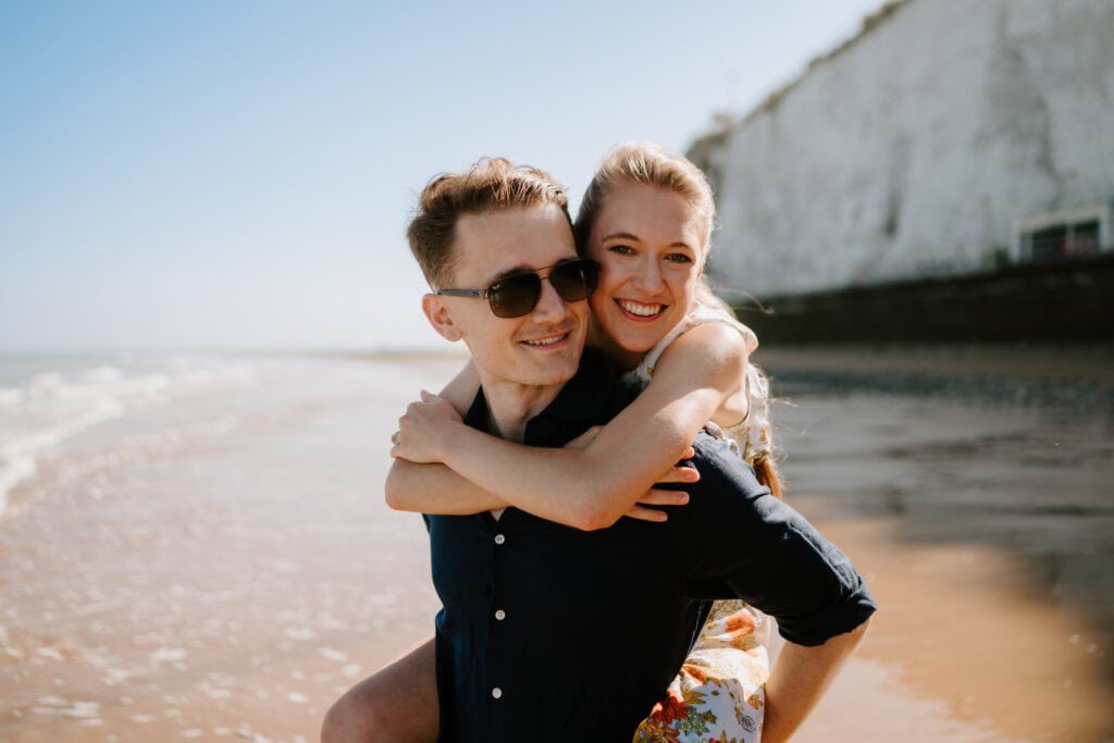 Couple enjoying piggyback ride on sunny beach.
