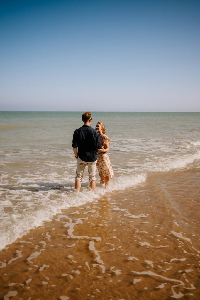 Couple standing in sea waves on sunny beach.
