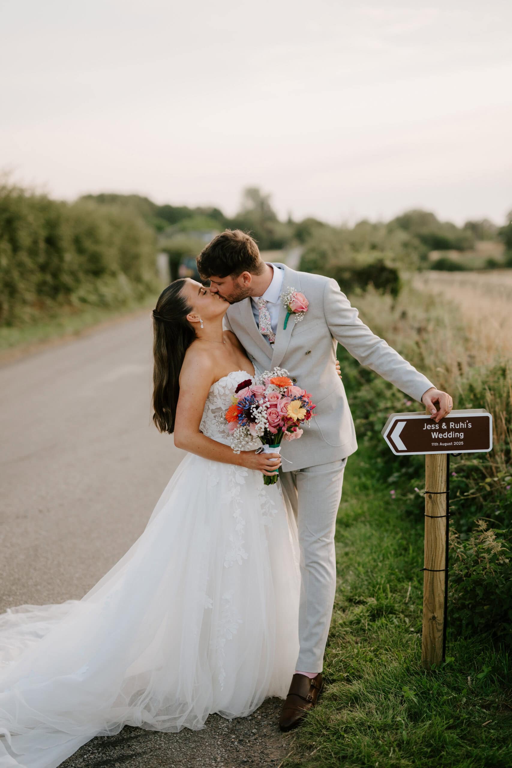 Bride and groom kissing by wedding signpost