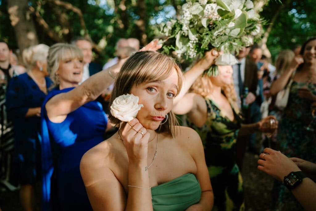 Woman holding a white rose at outdoor gathering.