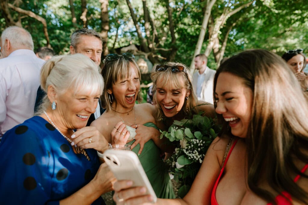 Group of women laughing at phone outdoors.