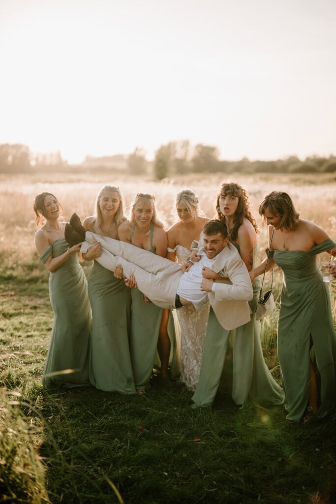 Bridesmaids lifting groom in a field