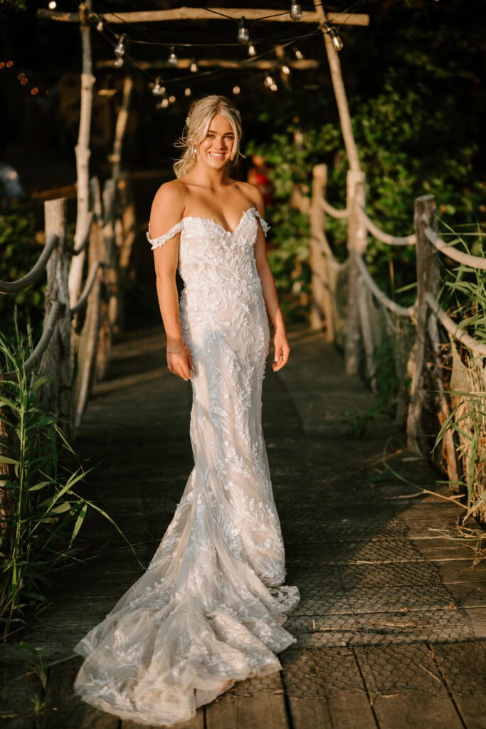 Bride in elegant lace wedding dress on wooden bridge.