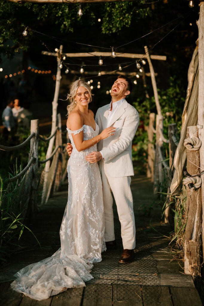 Happy couple laughing on rustic outdoor wedding bridge.