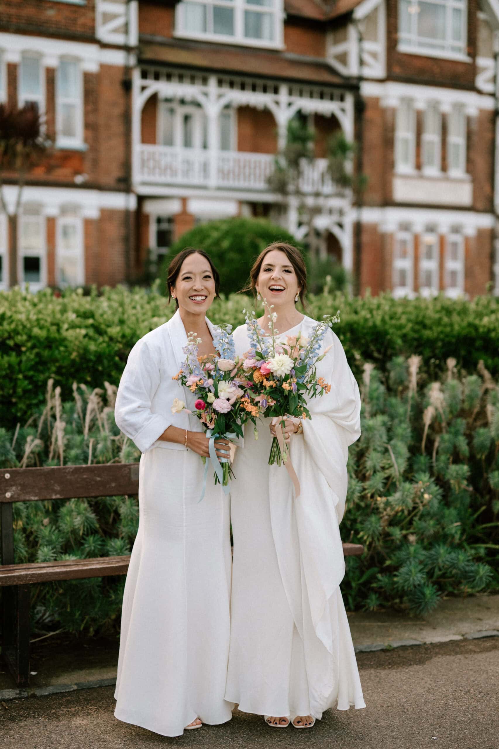 Two brides smiling with bouquets in garden setting