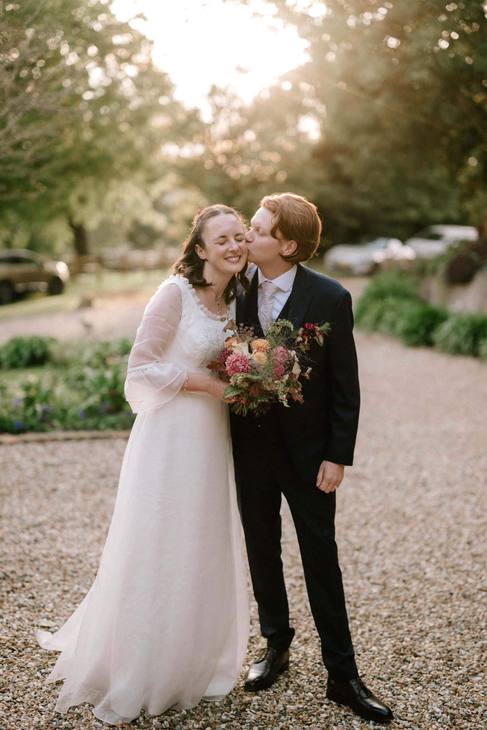 Bride and groom smiling, kissing outdoors.