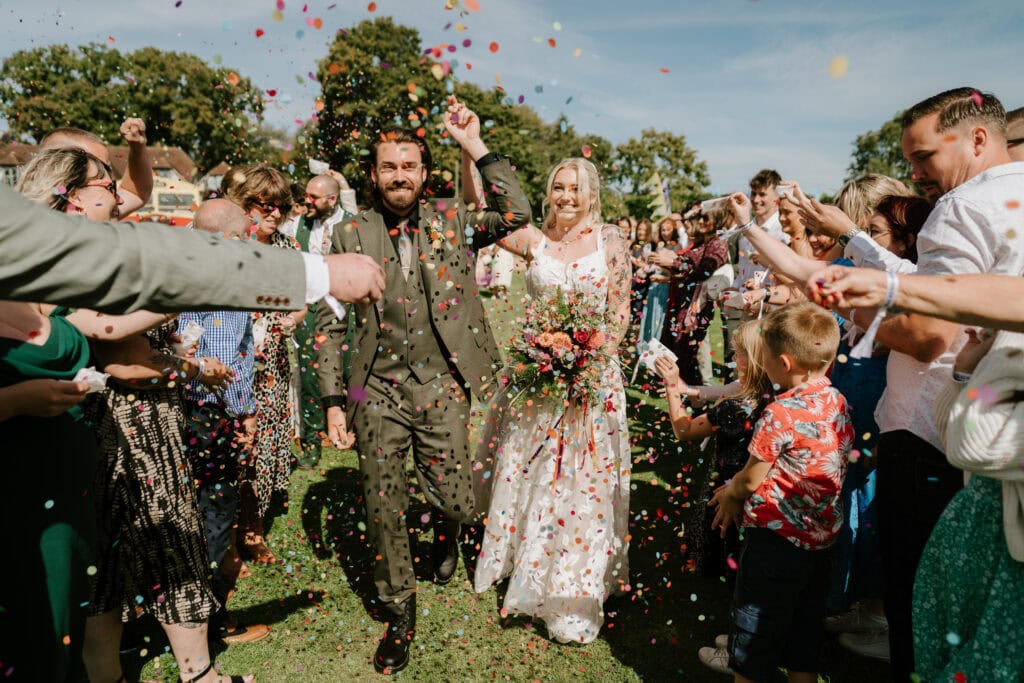 Bride and groom showered with confetti outdoors.