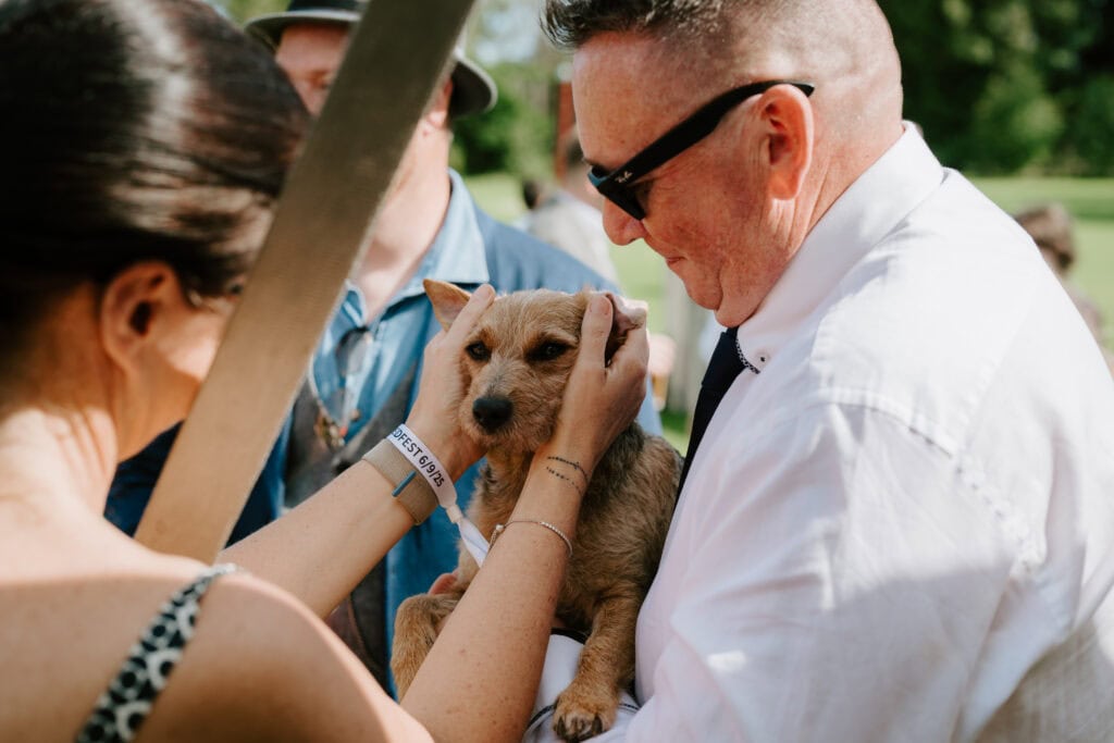 People holding a small brown dog outdoors.