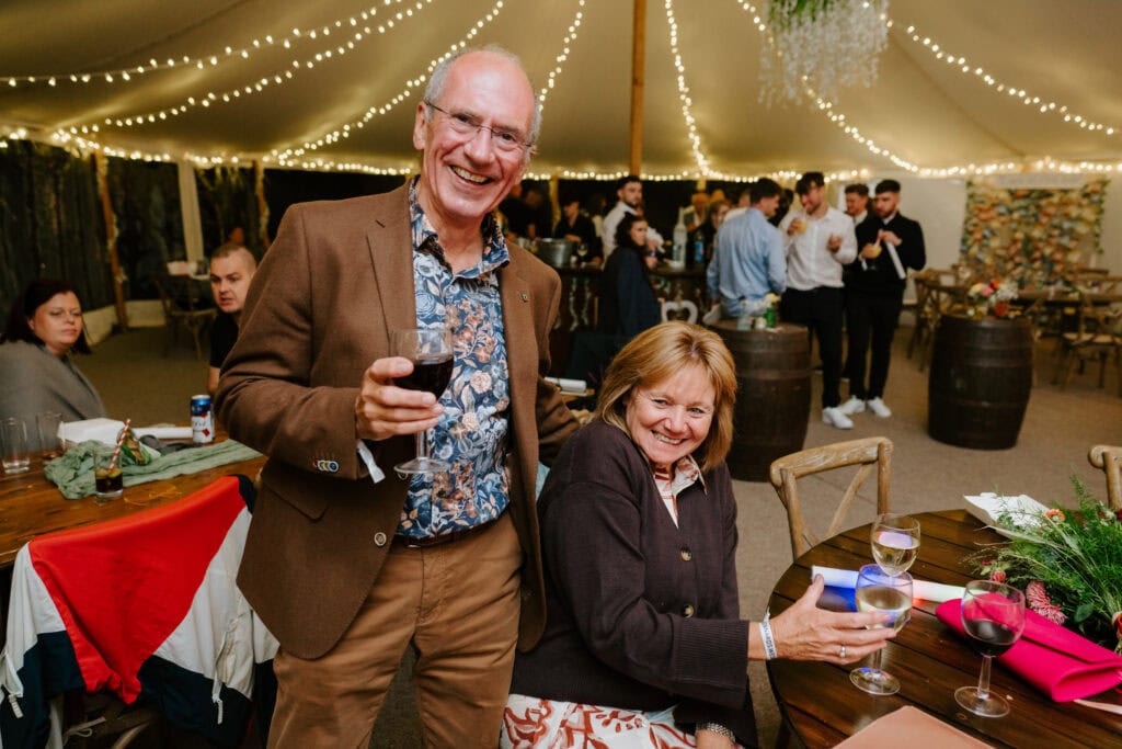 Smiling couple with wine at party, festive lights overhead.