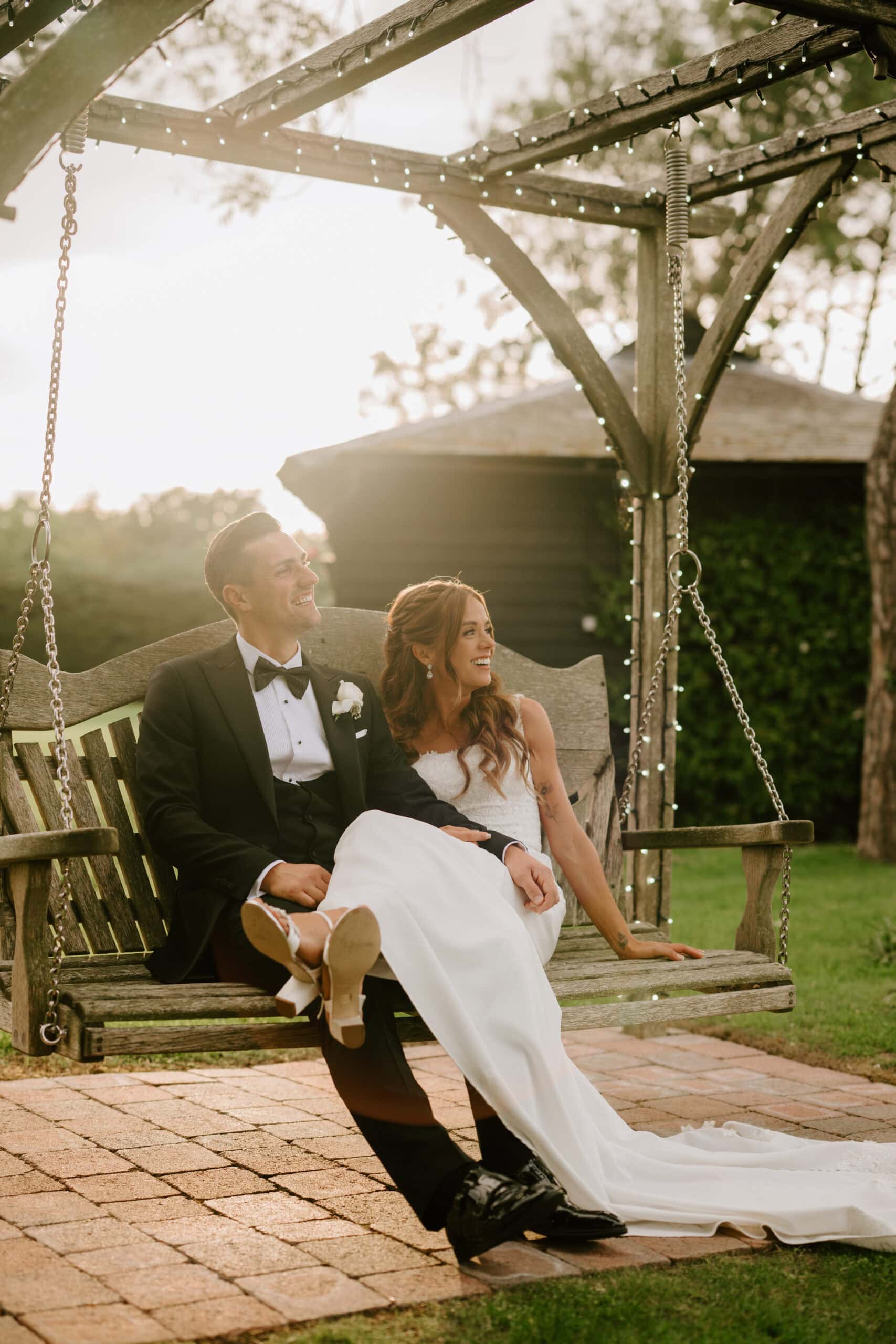 Bride and groom on garden swing, smiling joyfully.