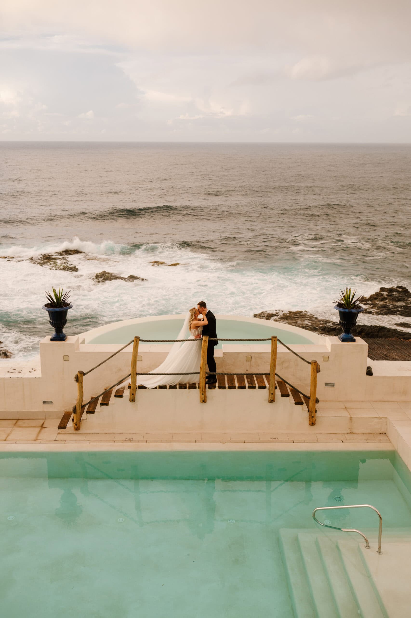 Bride and groom embrace by ocean view
