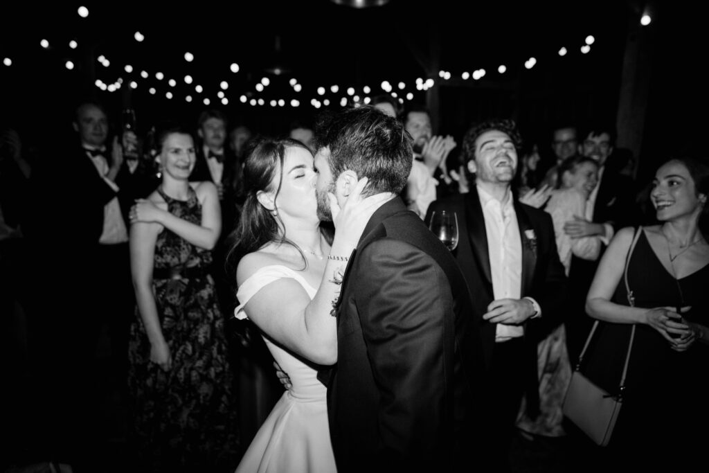 Couple kissing at party with joyful guests watching at updown farmhouse