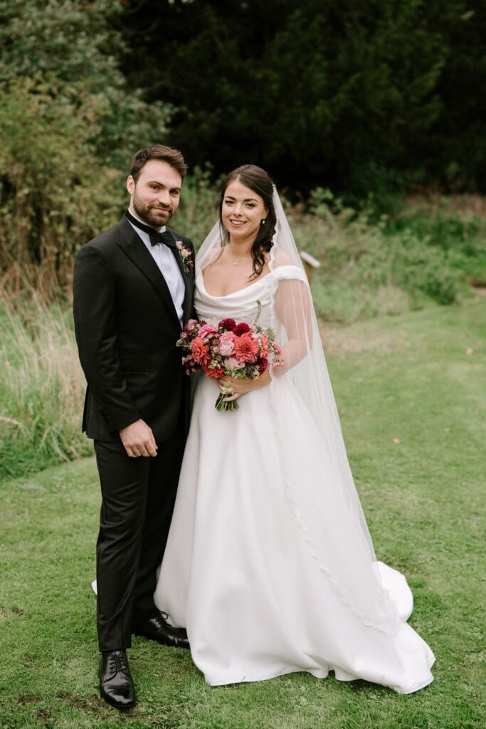 Bride and groom standing on grass outdoors.