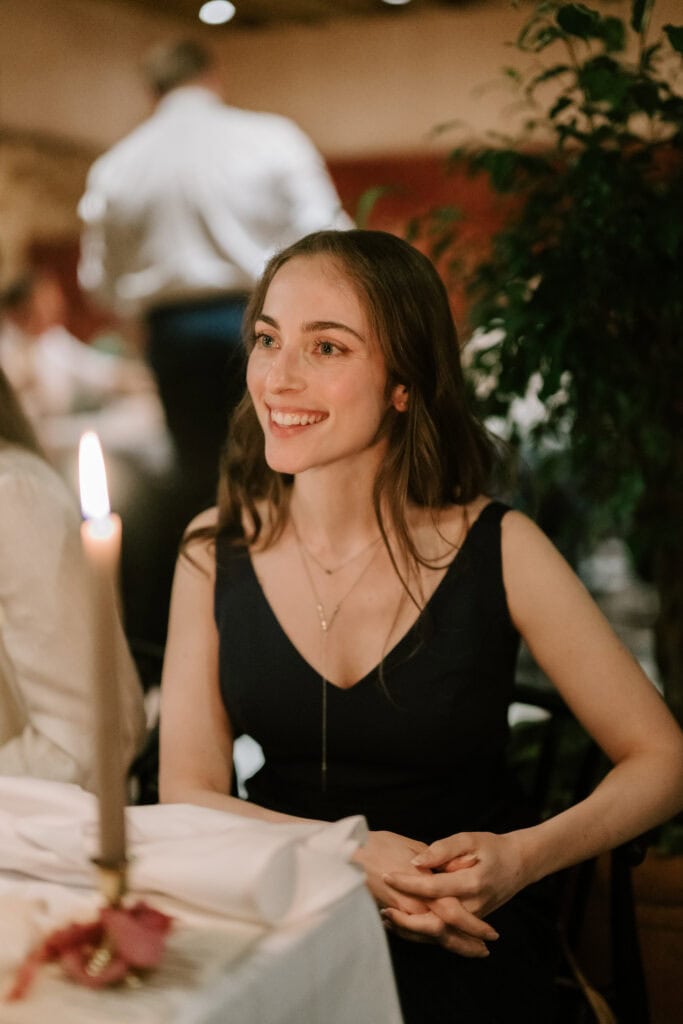 Smiling woman at candlelit dinner table.