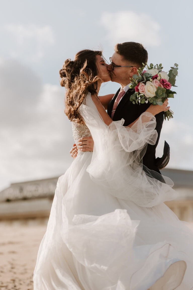 Newlyweds kissing on a windy ramsgate beach.