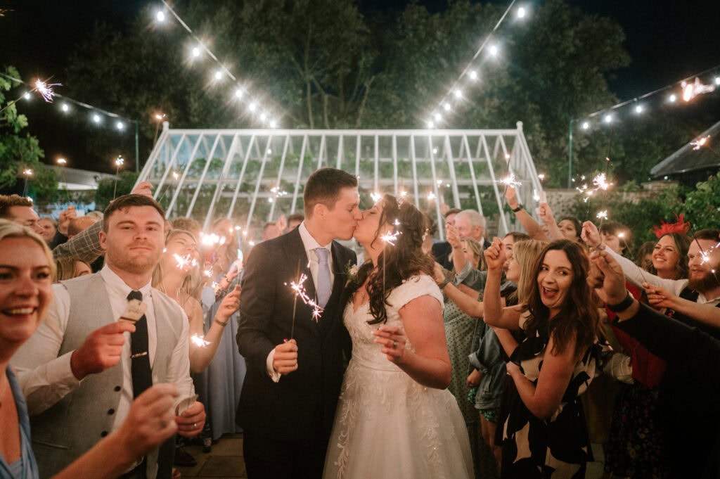 Bride and groom kissing surrounded by sparklers.