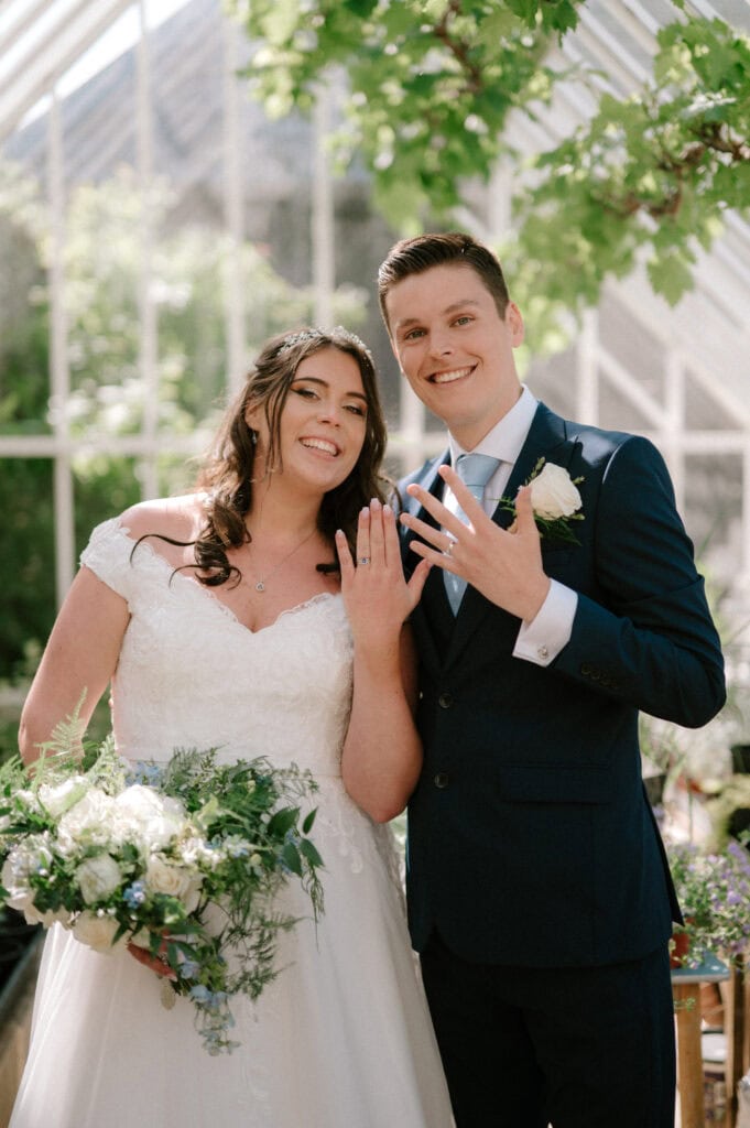 Bride and groom showing wedding rings in glass house at chapel house estate