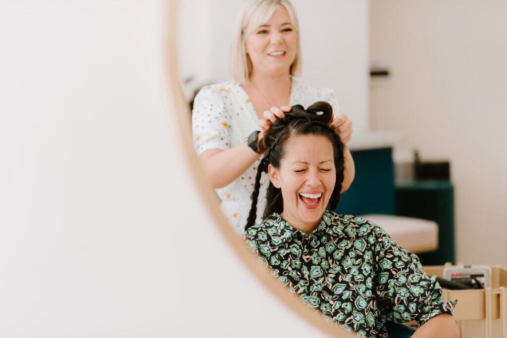 Laughing woman having hair styled in salon mirror