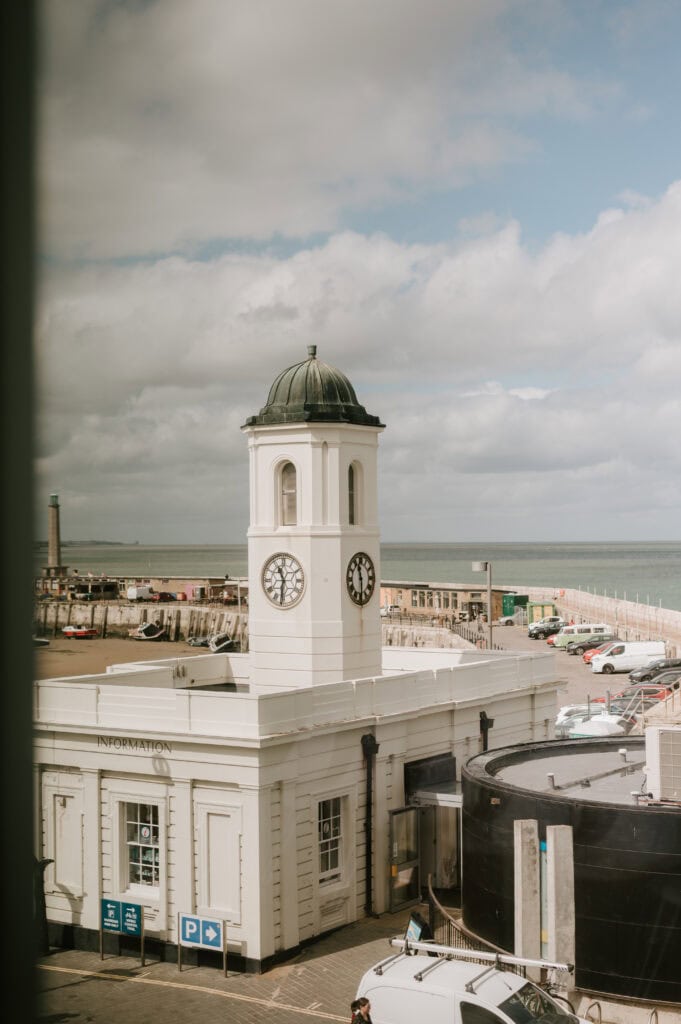 Clock tower by seaside with cloudy sky