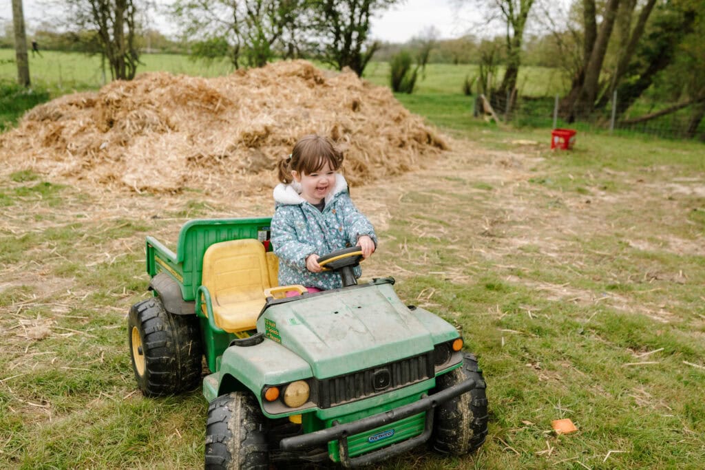 Child driving toy tractor near haystack