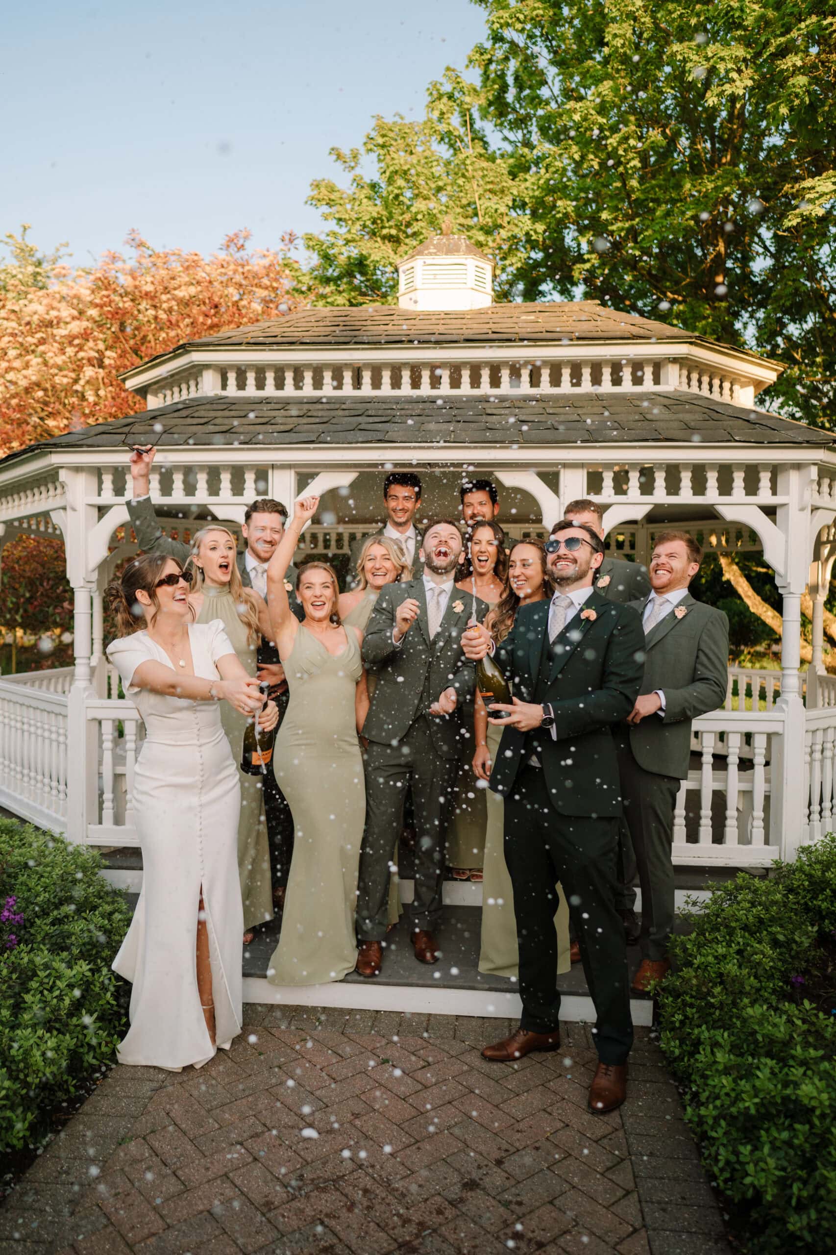 Wedding party spraying champagne outside garden gazebo