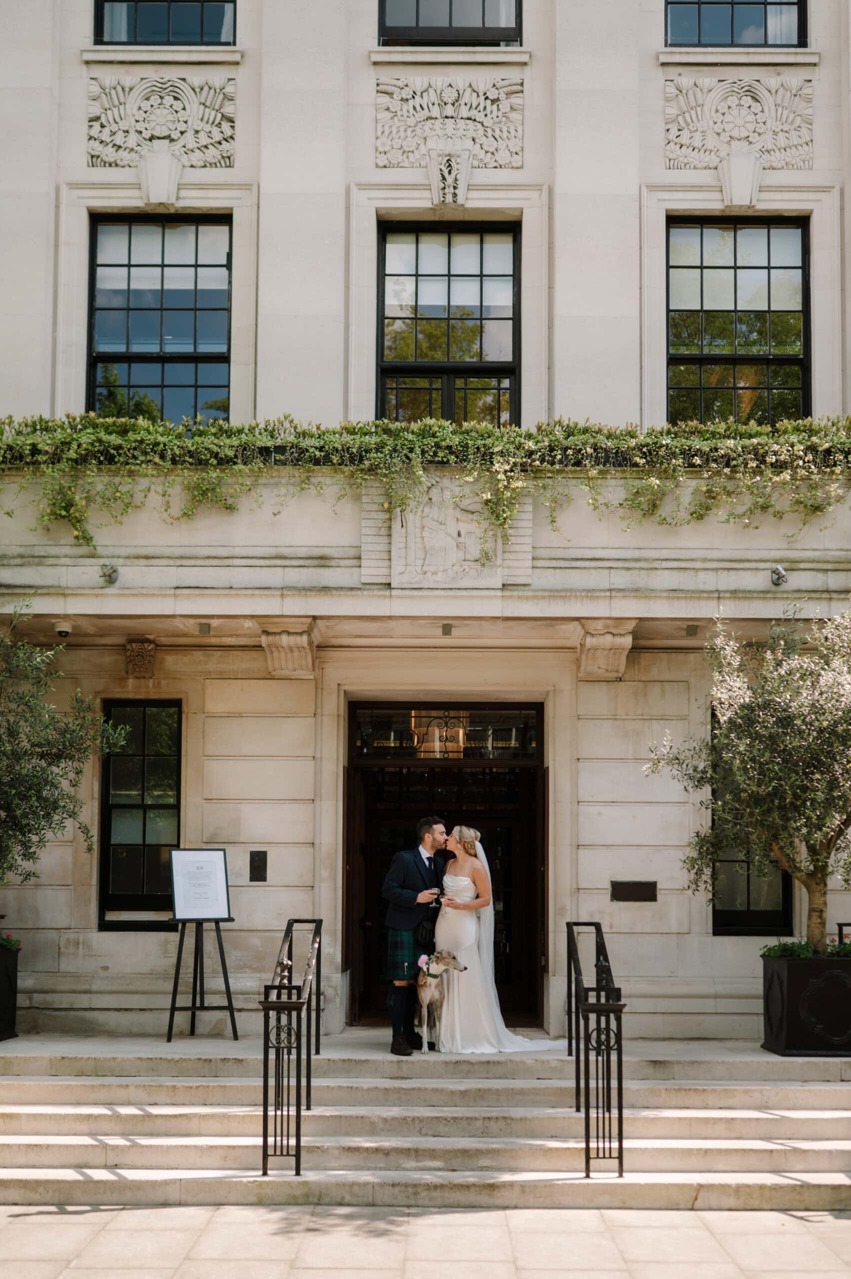 Bride and groom kissing with dog outside building