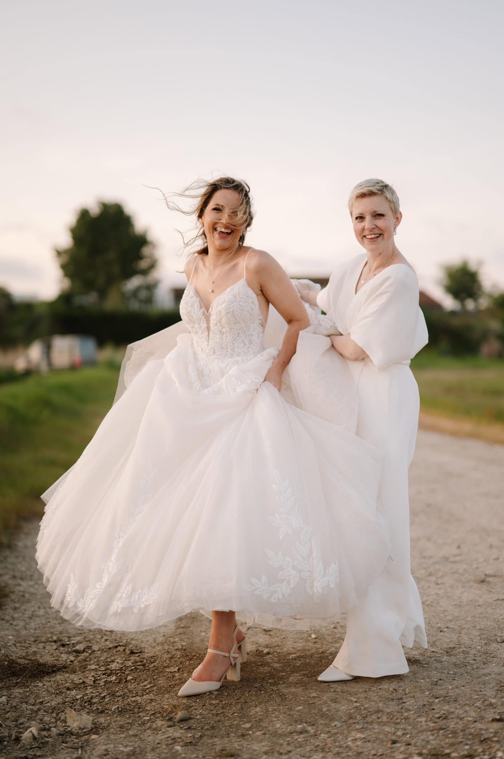 Bride and partner laughing outdoors in wedding dresses