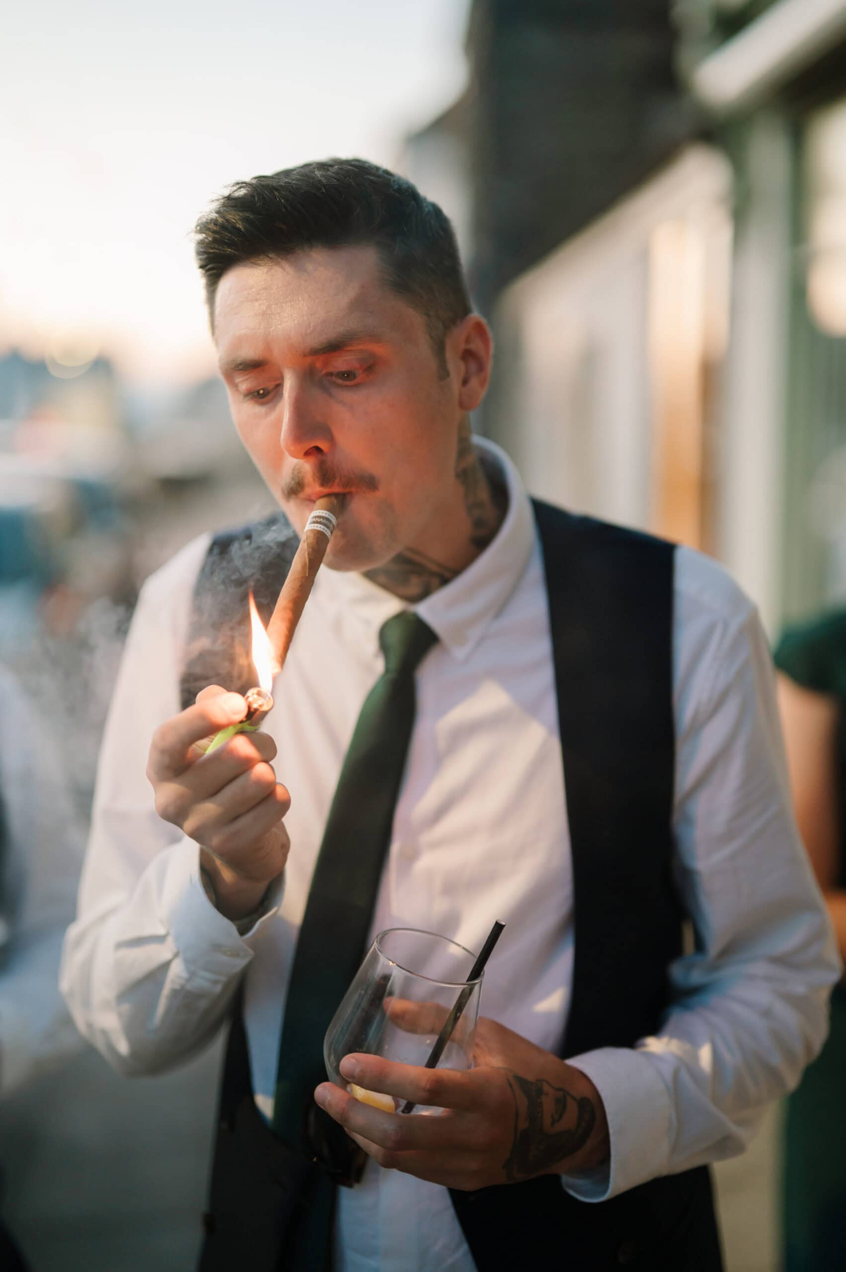 Man lighting cigar while holding drink outdoors