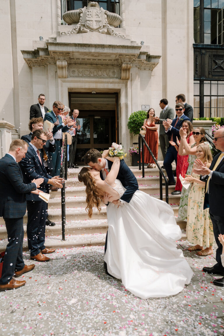 Bride and groom kiss on steps amid confetti