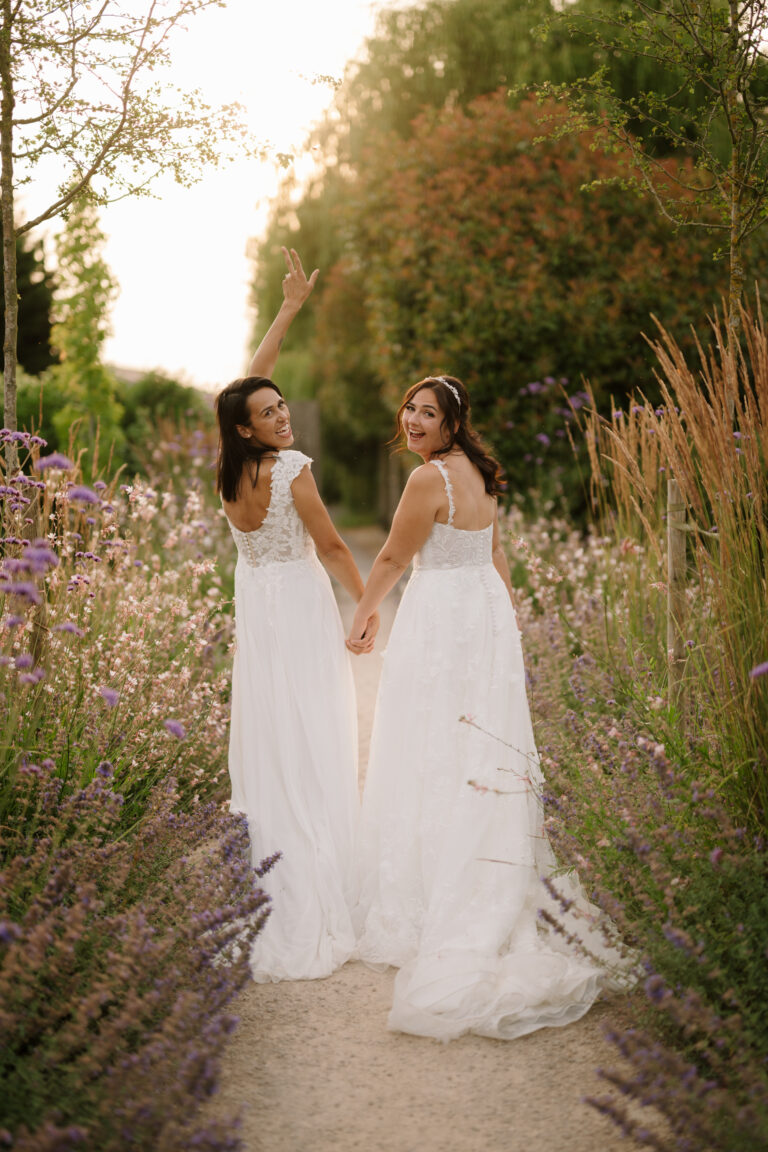 Two brides holding hands in flower garden at the old kent barn