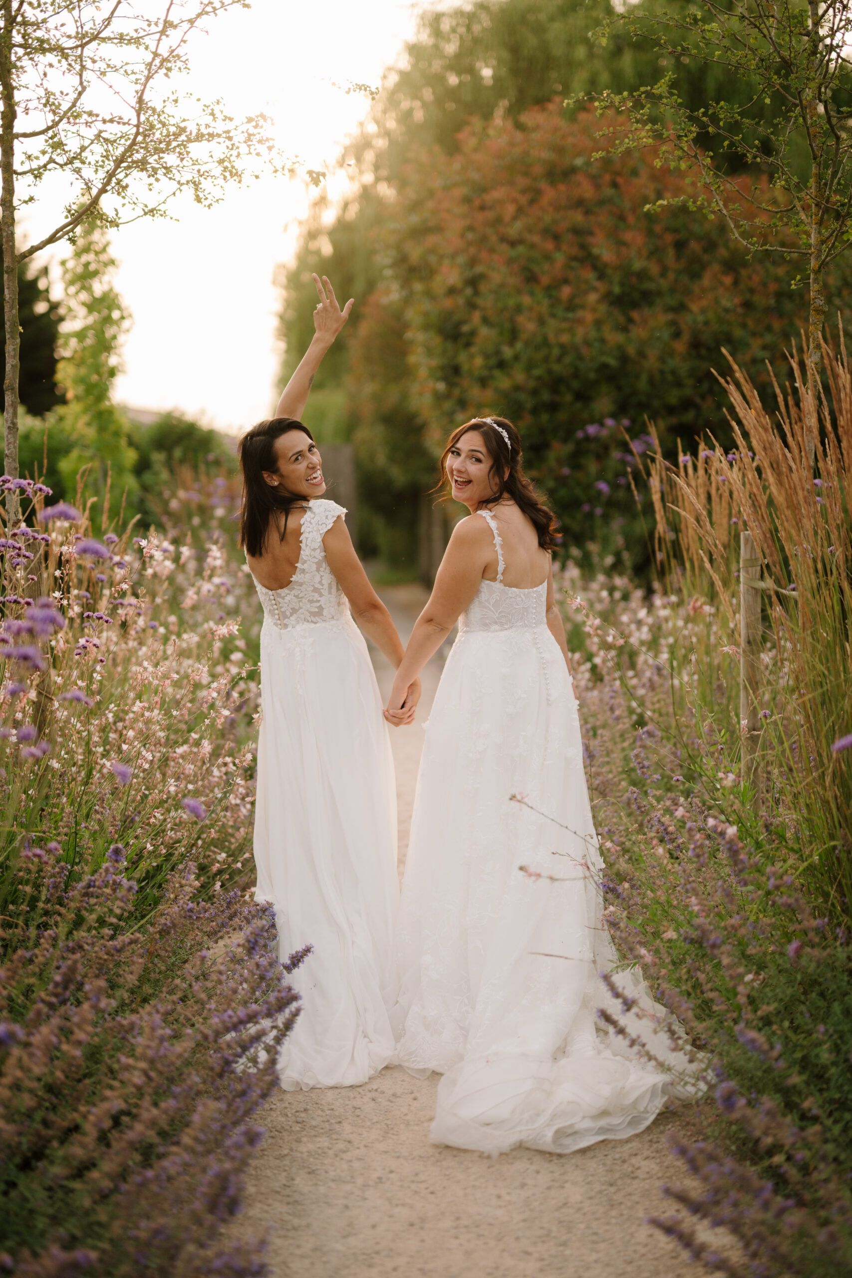 Two brides holding hands in flower garden at the old kent barn