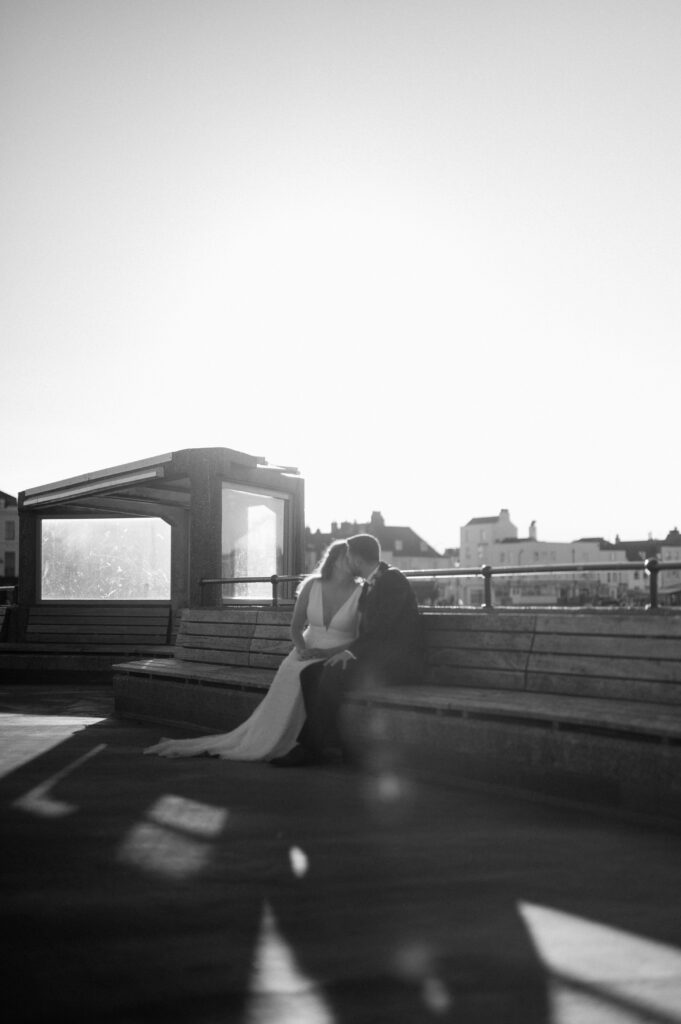 Bride and groom kissing on sunlit rooftop bench